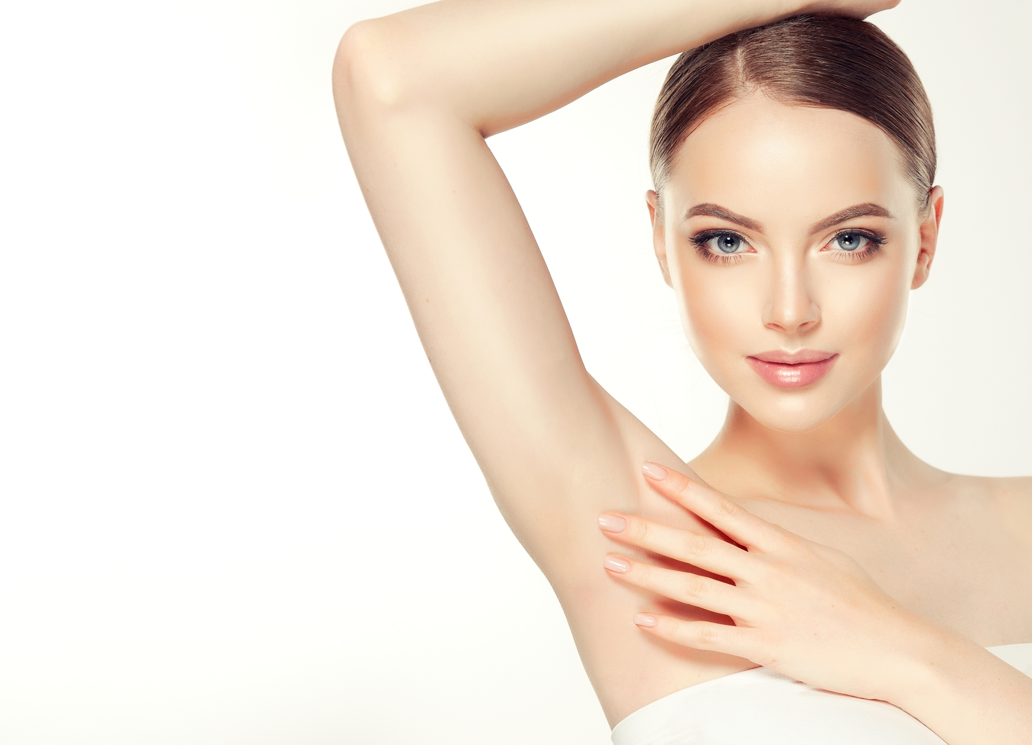 Gorgeous, young, brown haired woman with clean fresh skin and hair gathered in neat hairstyle is touching tenderly clean shaved armpit. Soft make up and light smile on the perfect face. Depilation, cosmetology and beauty technologies.